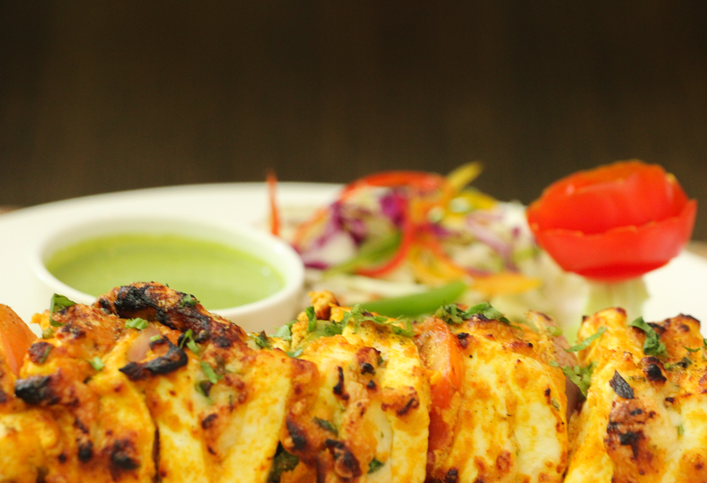 Paneer tikka skewers with charred edges on a plate